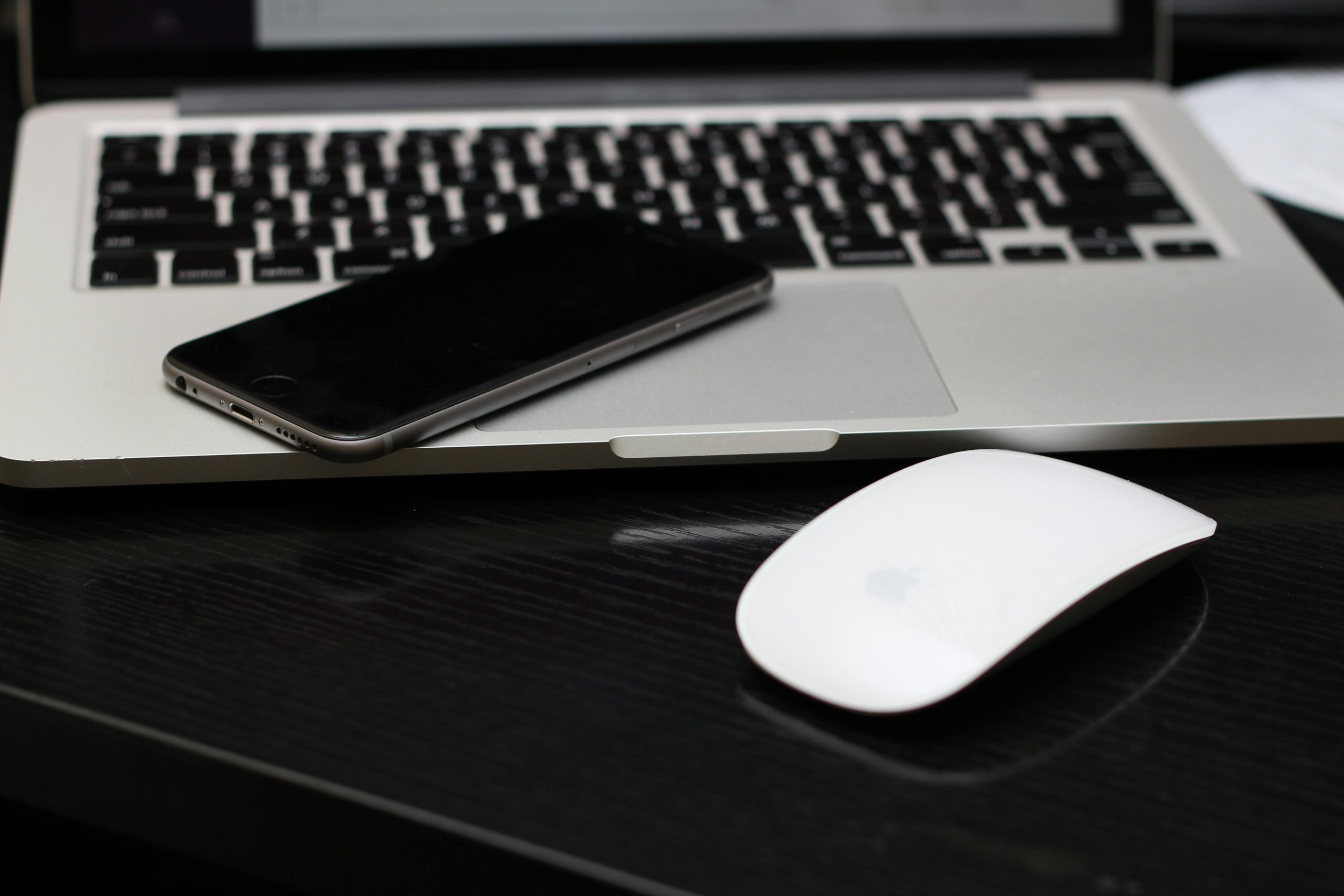 A sleek workspace featuring a laptop, smartphone, and wireless mouse on a desk.